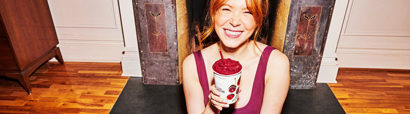 A woman sitting on a yoga mat holding a smoothie