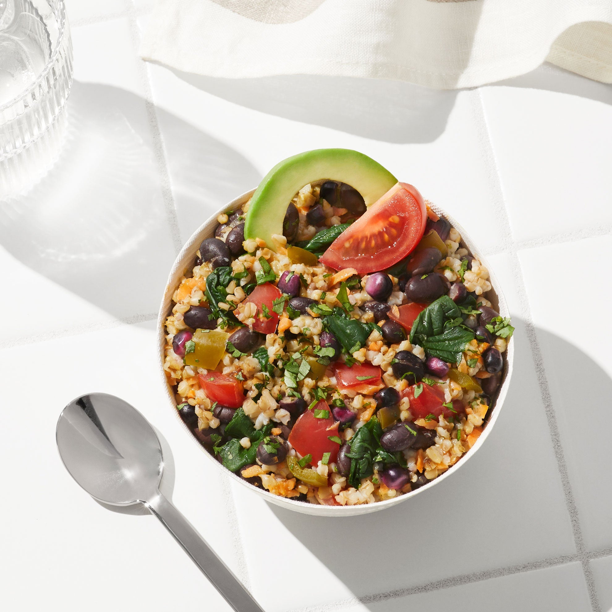 Overhead lifestyle image of Daily Harvest Black Bean + Tomatillo Oat Bowl prepared in a bowl with an avocado garnish.